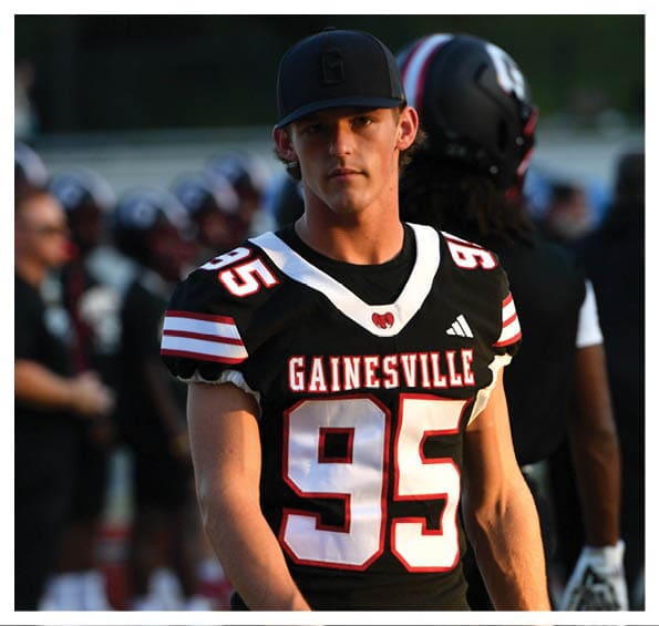 A person wearing a black Gainesville football jersey with the number 95 and a black cap stands on a field with other people in the background. Description generated by AI