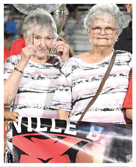 Four adults wearing red shirts stand together smiling behind a large banner with handwritten messages and the partial text “Farewell to F" and a date. Description generated by AI
