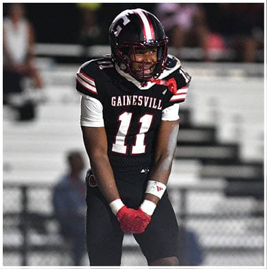 A person wearing a Gainesville football uniform with the number 11 is standing on a field with hands clasped and wearing red gloves. Description generated by AI