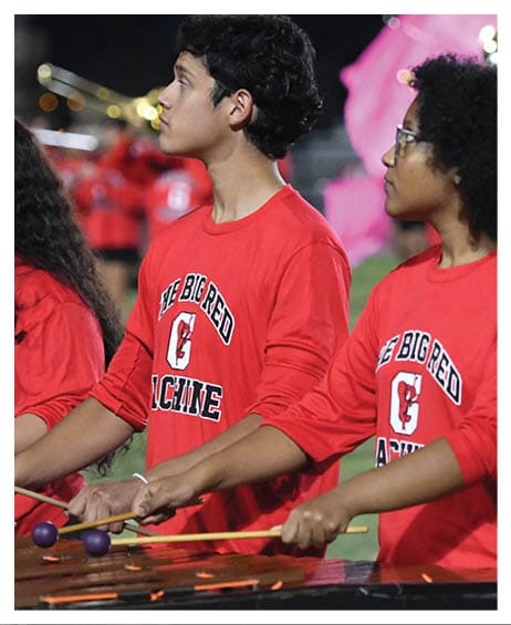 People wearing red shirts with “The Big Red" text are standing outdoors, with one person holding a pink flag in the background. Description generated by AI
