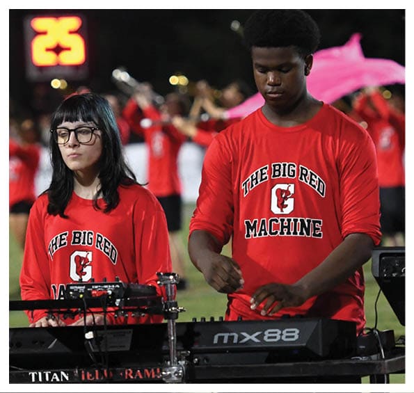People wearing red shirts with “The Big Red Machine" printed on them are playing musical instruments outdoors at night. Description generated by AI