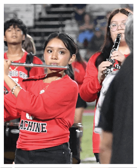 People wearing red shirts are playing musical instruments on a field while two others in dark clothing stand in the foreground. Description generated by AI
