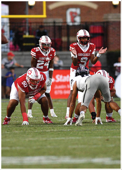 People in football uniforms are positioned on a field preparing for a play during a game. Description generated by AI