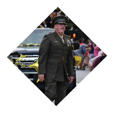 A person wearing a dark suit and polished shoes is walking across a street with a vehicle partially visible in the background. Description generated by AI