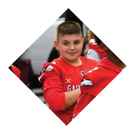 Children wearing red Gainesville sports jerseys are gathered outdoors, with one holding a black bucket. Description generated by AI