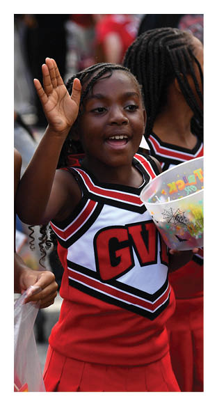 Two children wearing red and white cheerleading uniforms are engaged in an energetic moment, with one holding a plastic bag filled with items and the other raising a hand. Description generated by AI