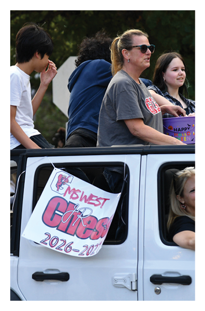 Several people are sitting and standing in a white vehicle with a sign on the door that reads “Midwest Cross 2026-2027." Description generated by AI