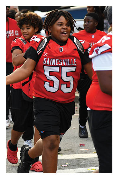 A person wearing a red Gainesville football jersey with the number 55 is walking energetically among others in similar sports attire. Description generated by AI