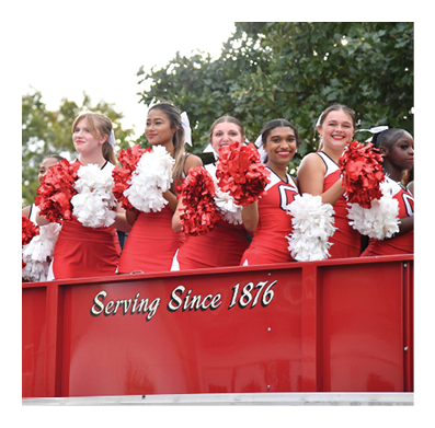 A person wearing dark pants is sitting on the edge of a bright red vehicle or container with the words “Serving Since 1876" written on it. Description generated by AI