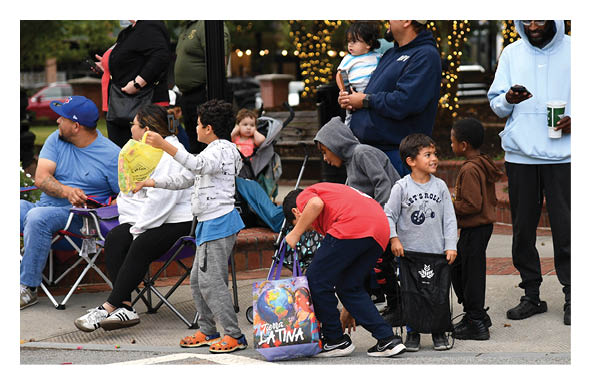 Children are gathered outdoors with one child smiling and wearing a sweatshirt that says “LET'S ROLL" while adults stand nearby, one holding a phone. Description generated by AI