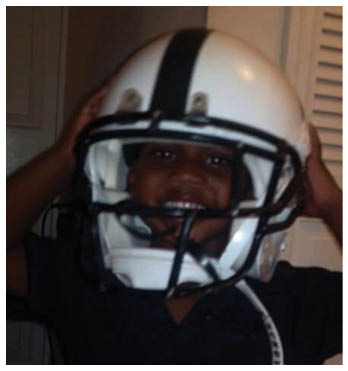A child is smiling while wearing a large white football helmet with a black stripe down the center. Description generated by AI