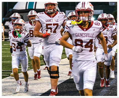 A group of people in white football uniforms with “Gainesville" on the jerseys are running on a field, with one person wearing a knee brace and others holding mouthguards. Description generated by AI