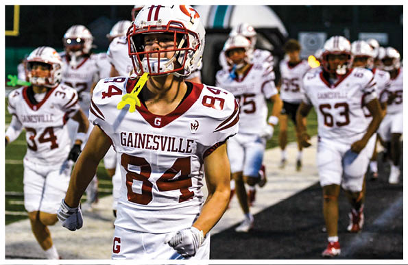 A group of people in white football uniforms with “Gainesville" on the jerseys are running on a field, with one person in the foreground wearing number 84. Description generated by AI
