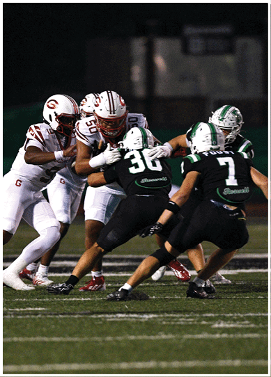 Two football players in white uniforms are blocking while two players in black uniforms attempt to tackle during a game on a grassy field. Description generated by AI