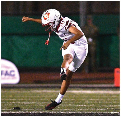 A person in a white football uniform is kicking a ball on a field during a nighttime game. Description generated by AI