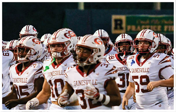 A group of people wearing white football uniforms with “Gainesville" written on them are standing together on a field. Description generated by AI