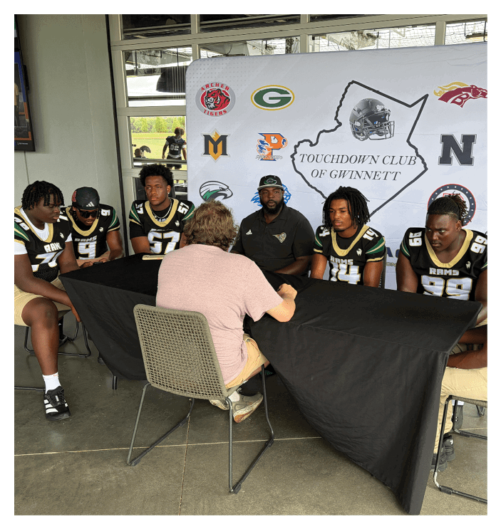 A football game is in progress with players on the field. One player is throwing a football while another player is trying to catch it. The players are wearing uniforms and are actively engaged in the game. AI generated content