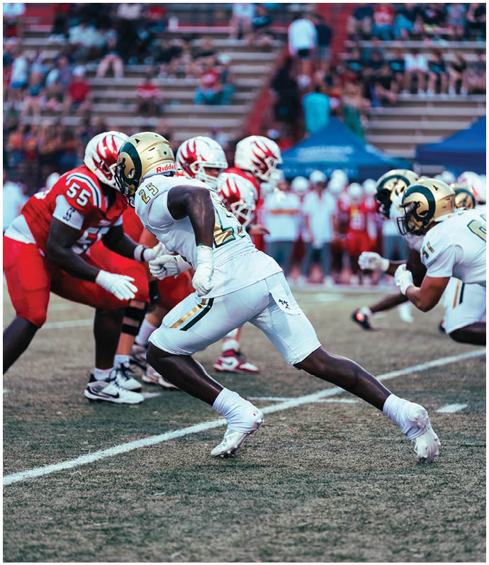 Three football players in blue and white uniforms running on a field. Description generated by AI