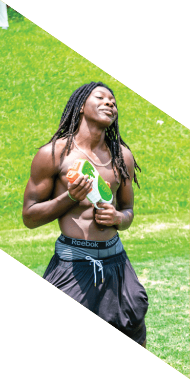Two football players are on the field, one jumping in the air while the other is running. A referee is also present, watching the play. AI generated content