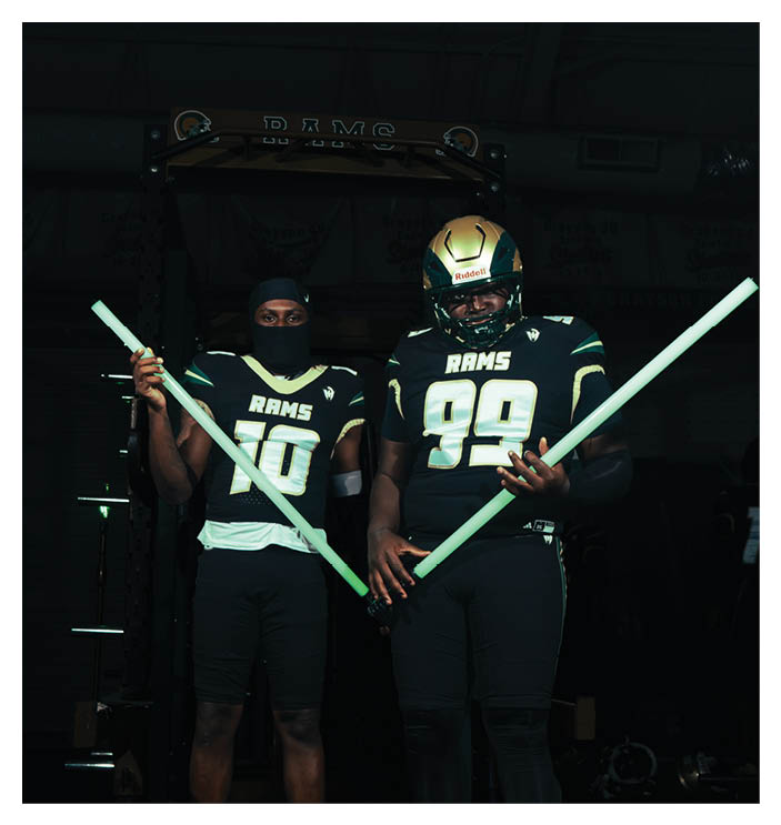A football game is in progress with players on the field. One player is throwing a football while another player is trying to catch it. The players are wearing uniforms and are actively engaged in the game. AI generated content
