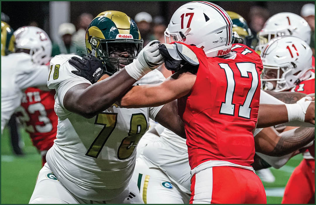 Two football players in helmets and uniforms are engaged in a physical block during a game on a green field. Description generated by AI