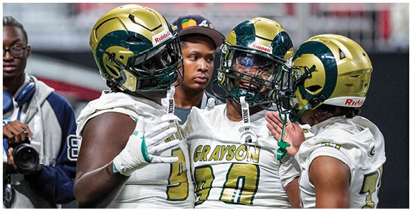 Three people in football uniforms and helmets are standing close together on a field, with one person holding a football. Description generated by AI