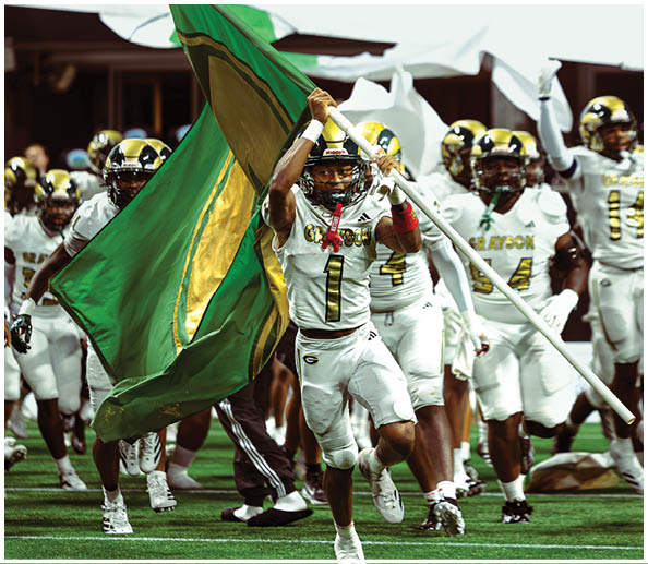 People wearing helmets are holding up a green flag with a yellow circle in the center, with a large white banner featuring red markings in the background. Description generated by AI