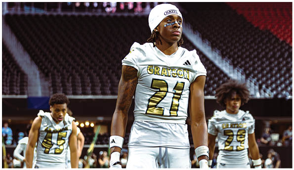 A person wearing a white beanie and face paint stands inside Mercedes-Benz Stadium with a large screen and empty seats in the background. Description generated by AI