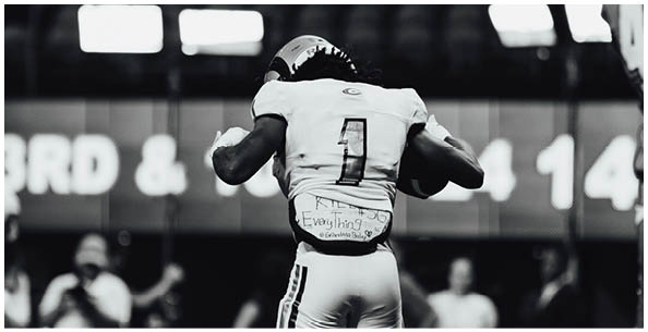 A person wearing a helmet and sports gear is seen from behind in a stadium with empty seats. Description generated by AI