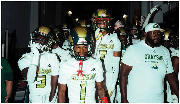People wearing white football uniforms with “Grayson" written on them stand together indoors. Description generated by AI
