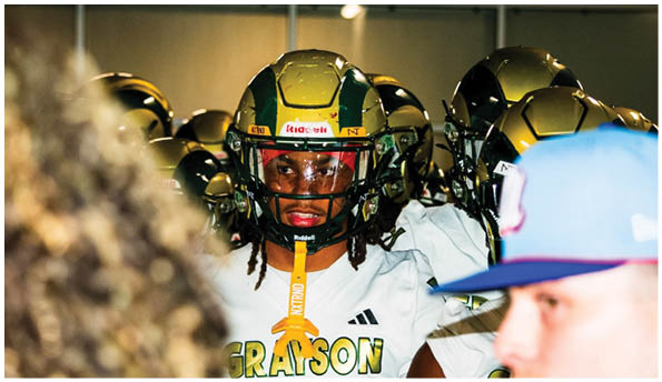 A group of people wearing gold and green football helmets and white uniforms are gathered closely together indoors. Description generated by AI