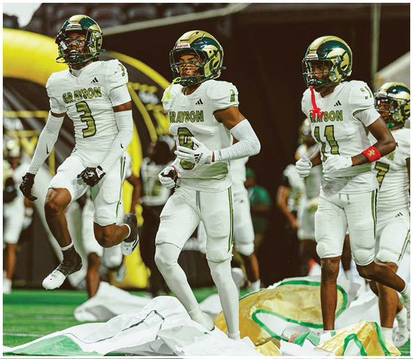 Three people wearing white football uniforms with gold helmets and the word Grayson on their jerseys stand on a field during a game. Description generated by AI