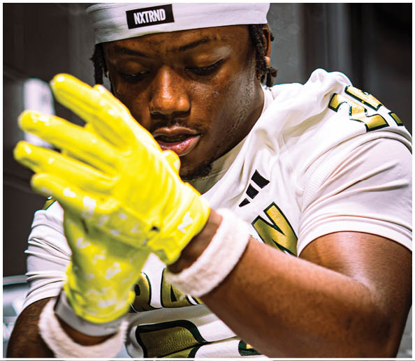 A person wearing a white sports jersey with gold and black details is putting on bright yellow gloves and has white wristbands on both wrists. Description generated by AI