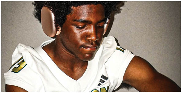 A person wearing a white sports jersey with the word “GRAYSON" and the number 13 is looking down with a focused expression. Description generated by AI