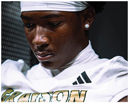 A person wearing a white sports jersey with gold and black lettering and an Adidas logo is shown from the shoulders to the chest. Description generated by AI