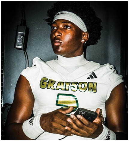 A person wearing a white football uniform with “GRAYSON" and the number 2 on the jersey is holding a smartphone while sitting down. Description generated by AI