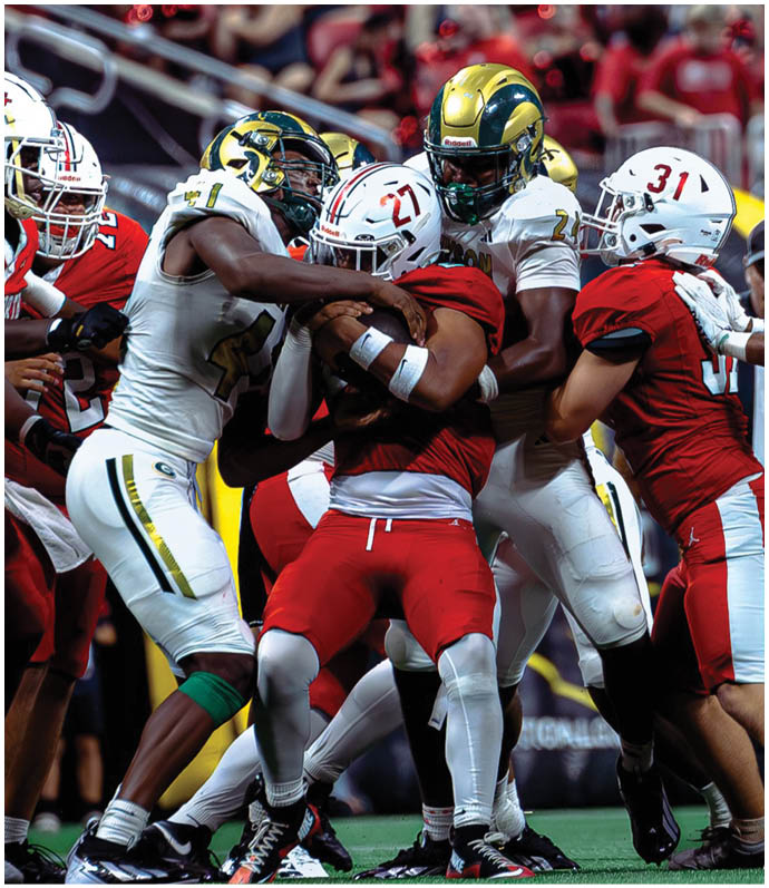 Several people wearing football uniforms are engaged in a close physical struggle on a field during a game. Description generated by AI