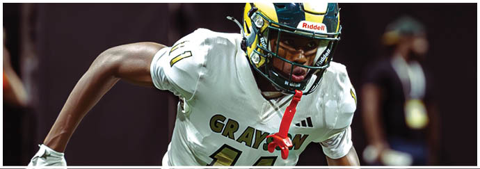 A person wearing a white sports uniform with yellow and black stripes is running on a green field while holding a football. Description generated by AI