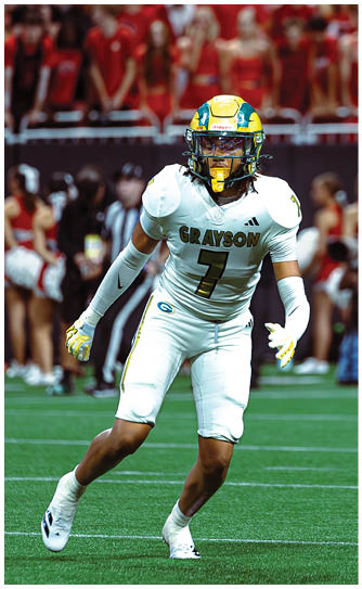 A person wearing a white football uniform with the name Grayson and number 7 is running on a green field during a game with a crowd in the background. Description generated by AI