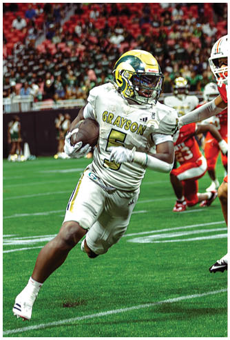 A person in a white and gold football uniform with the name Grayson and number 5 is running on a green field while holding a football, with other players in red uniforms in the background. Description generated by AI