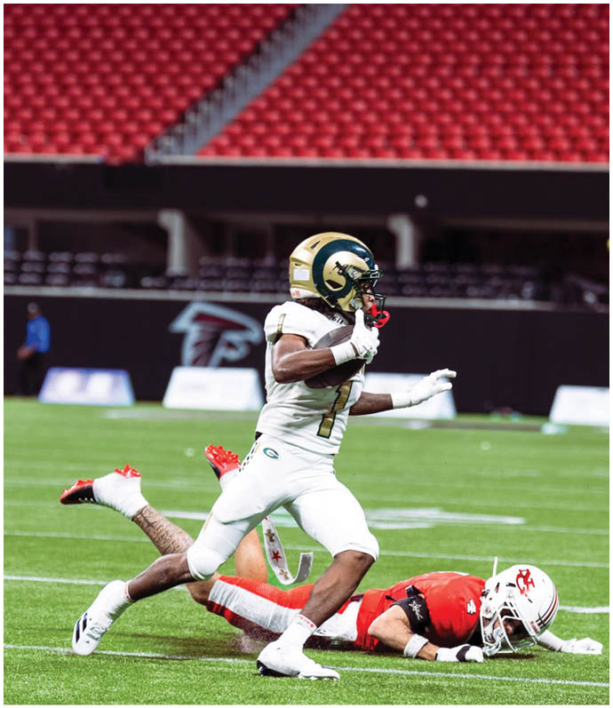 A person in a white football uniform is running on a field while another person in a red football uniform is lying on the ground behind them. Description generated by AI