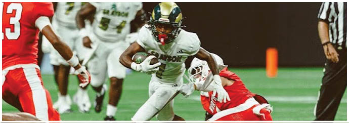 People in football uniforms are actively playing on a field with one person running while others are in pursuit and a referee is visible on the side. Description generated by AI