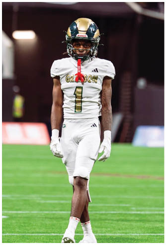 A person wearing a white football uniform with the number one and a gold and black helmet is walking on a green football field inside a stadium. Description generated by AI