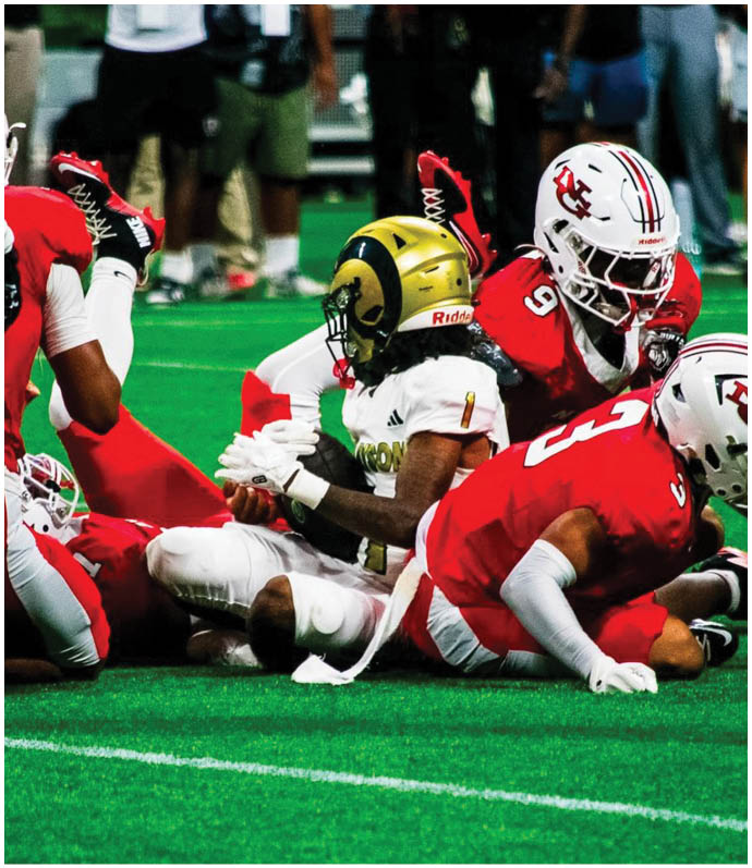 People in sports uniforms are lying on the ground on a green field with white lines, with one person standing nearby wearing white shoes. Description generated by AI