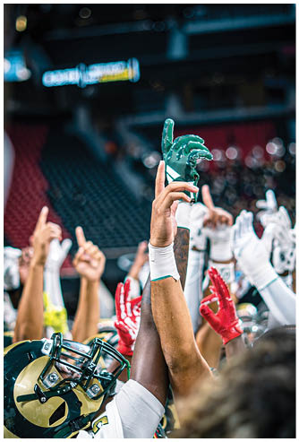 Several people wearing sports gloves and uniforms raise their hands together in a gesture of unity or celebration inside a stadium. Description generated by AI