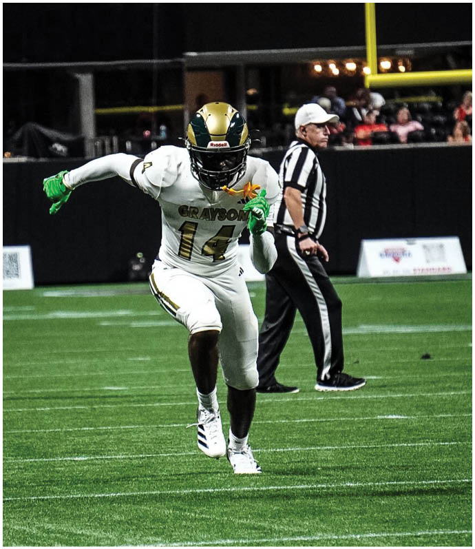 A person in a white football uniform with the number 14 and green gloves is running on a football field with a referee standing in the background. Description generated by AI