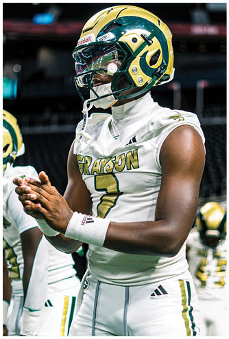 A person wearing a white football uniform with the name Grayson and number 7 is standing on a field with another player blurred in the background. Description generated by AI
