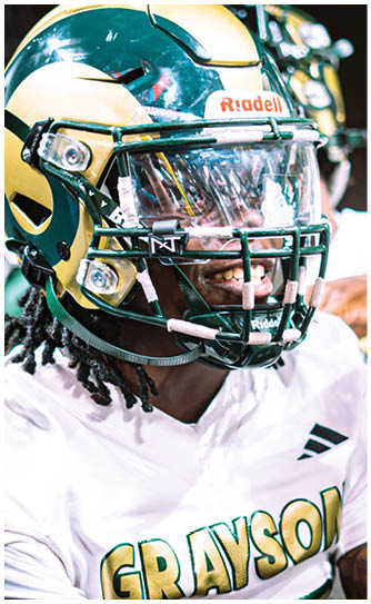 A person wearing a football helmet and a white jersey with the word “GRAYSON" smiles while looking to the side. Description generated by AI