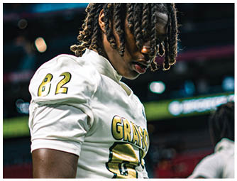 A person wearing a white sports jersey with the number 82 and the word “GRAYSON" in gold letters is standing in a stadium. Description generated by AI