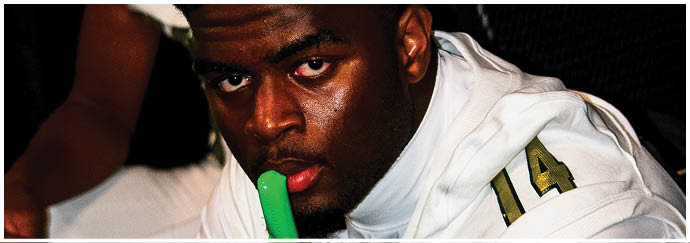 A person wearing a white sports jersey with the number 14 is holding a green mouthguard near their mouth. Description generated by AI